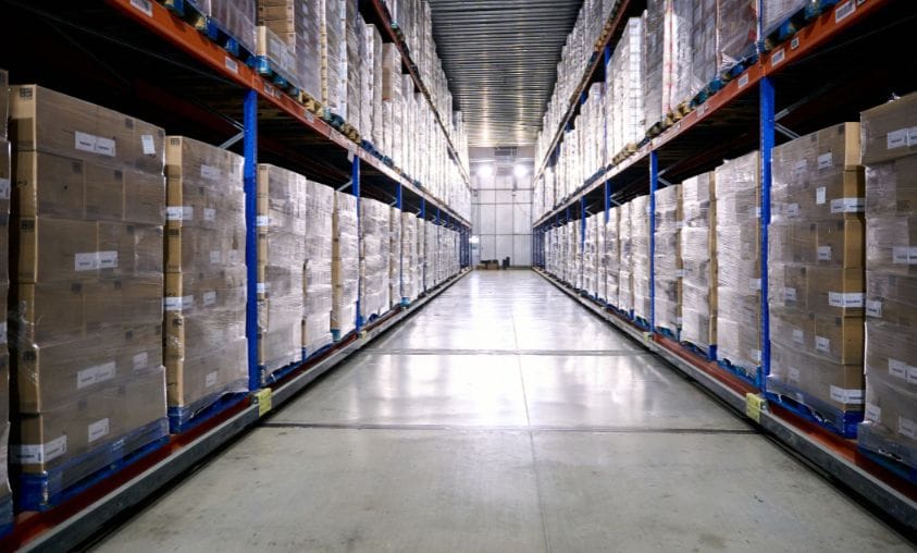 A wide aisle inside a cold storage warehouse with tall racks of palletized, shrink-wrapped goods on both sides, illustrating organized cold storage for food businesses.