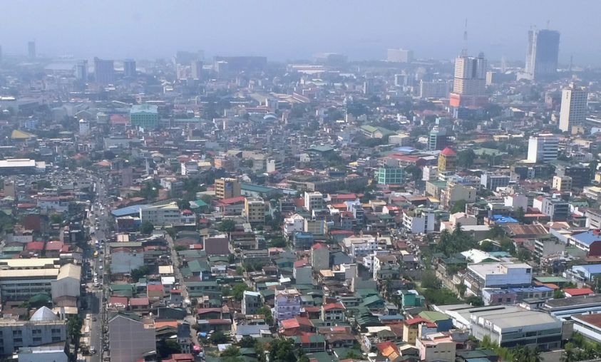 A hazy aerial view of a dense urban cityscape with closely packed buildings and high-rise structures, illustrating older city developments and the need for modern building upgrades.